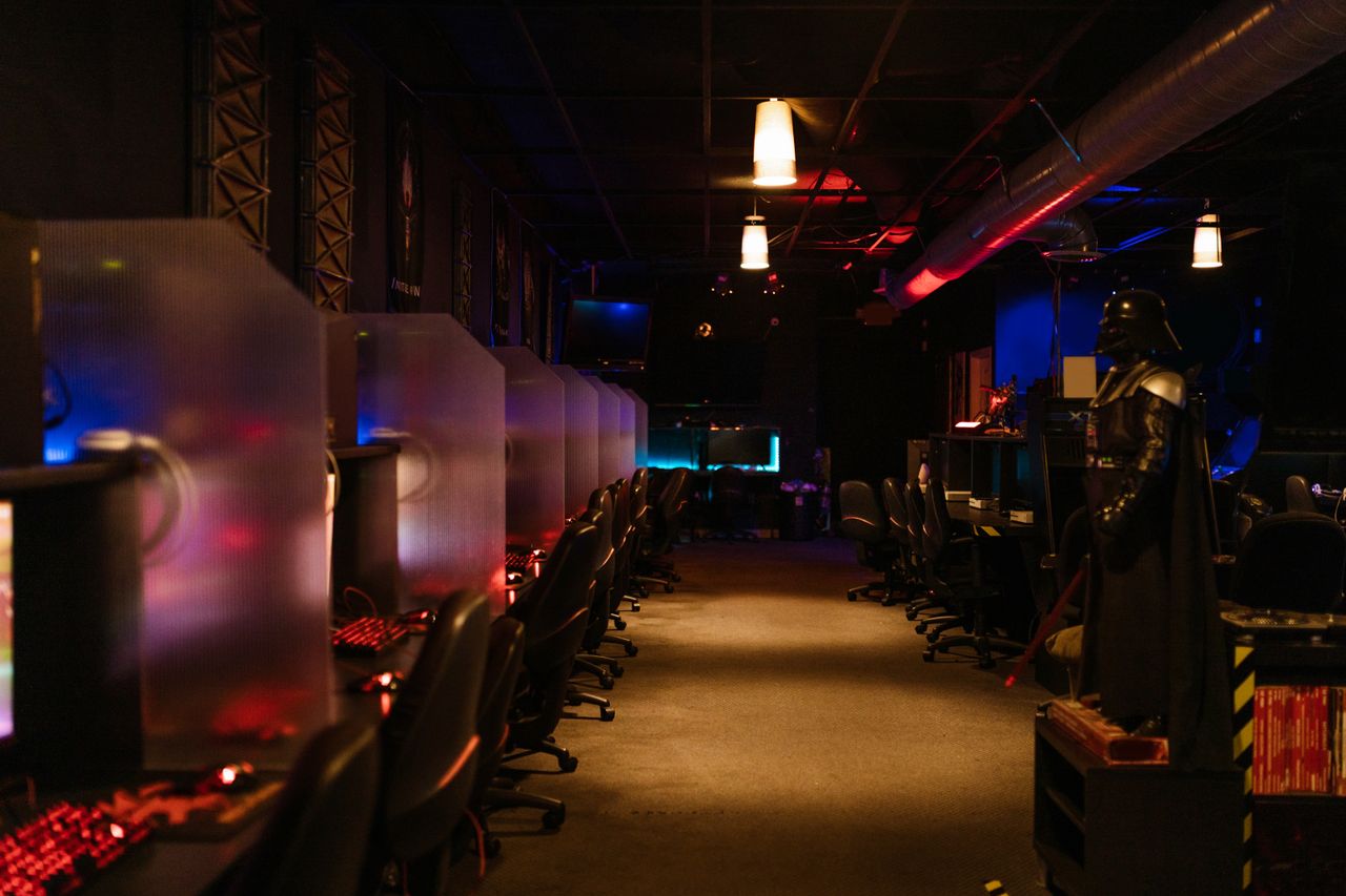 Services A dimly lit gaming arcade with neon lights and computers, creating a futuristic atmosphere.