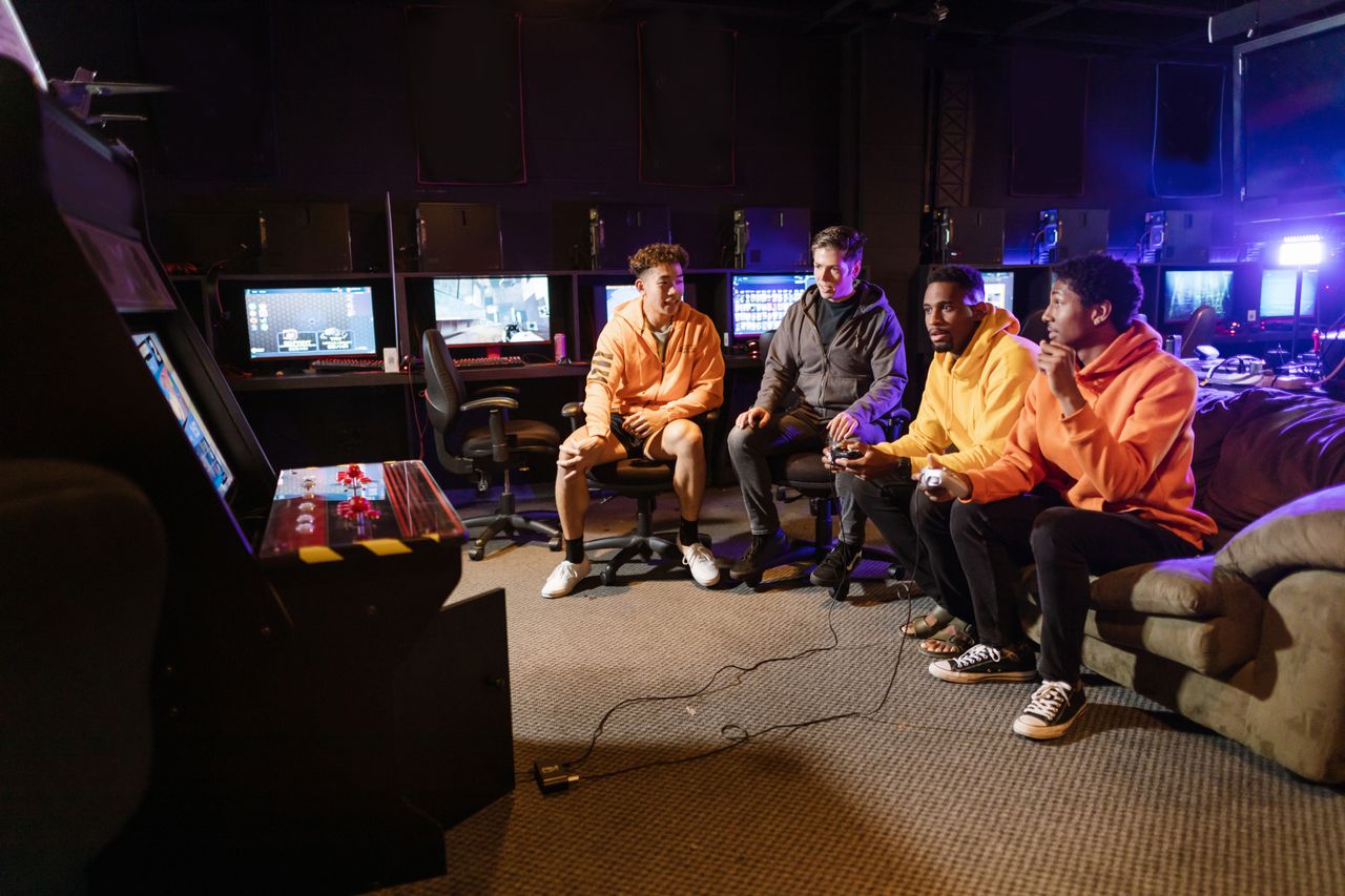 Services A group of young men having fun gaming together indoors, using controllers and arcade machines.